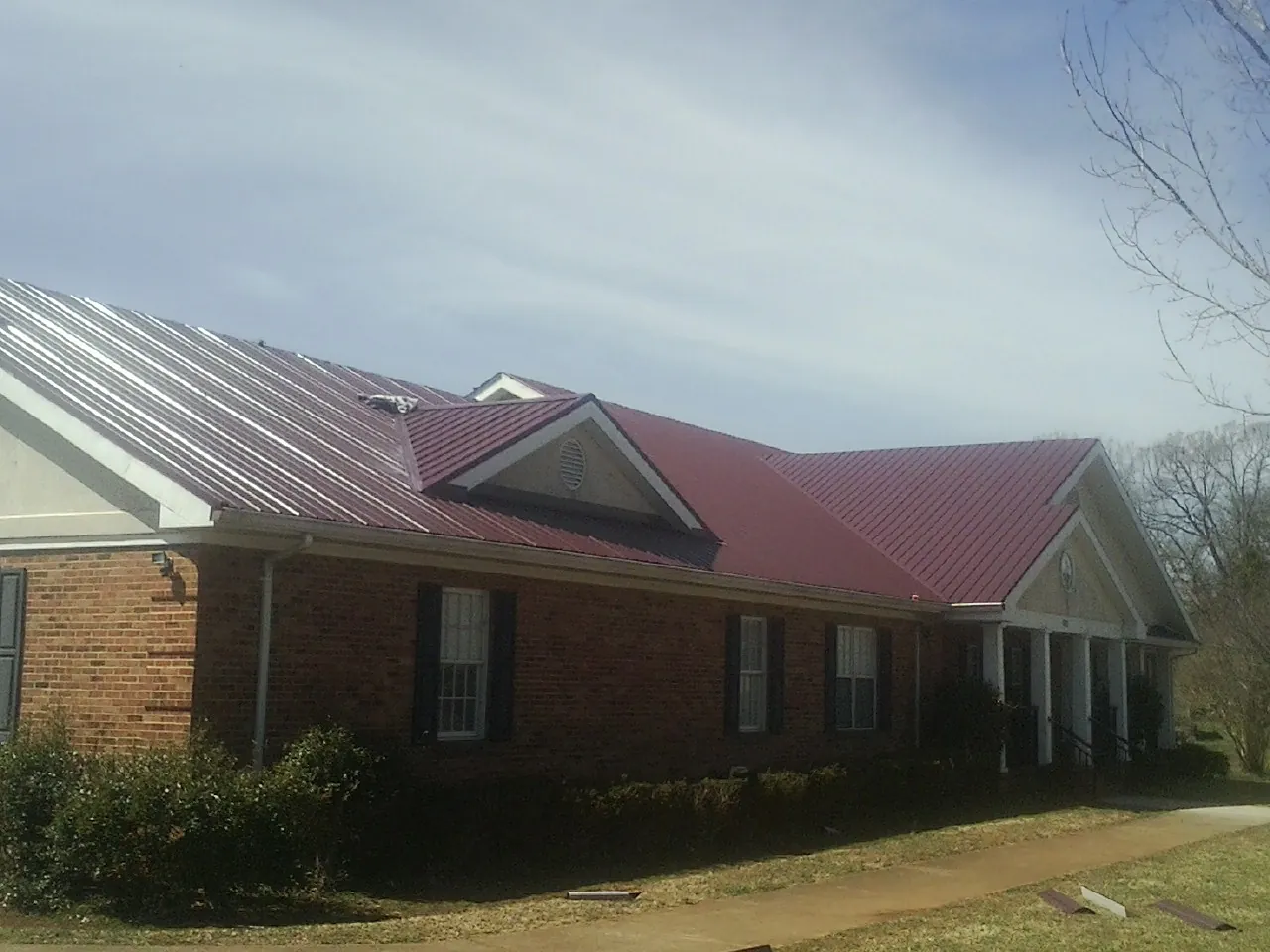 Red metal roof with gabled entries on a long brick building, from a Hail Damage Roof Repair job in Gwynedd