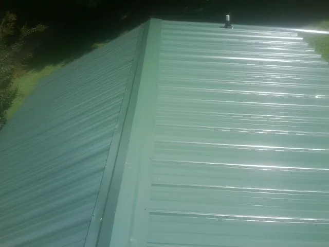 New green metal panels meeting at the ridge of a roof — Flat Roof Repair work by our crew in Gwynedd