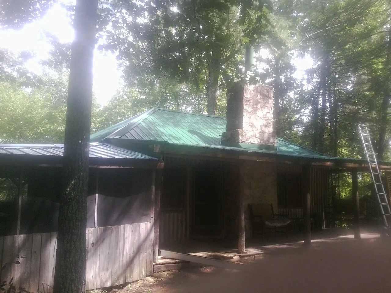 Green metal roof and stone chimney above a log cabin porch in Gwynedd