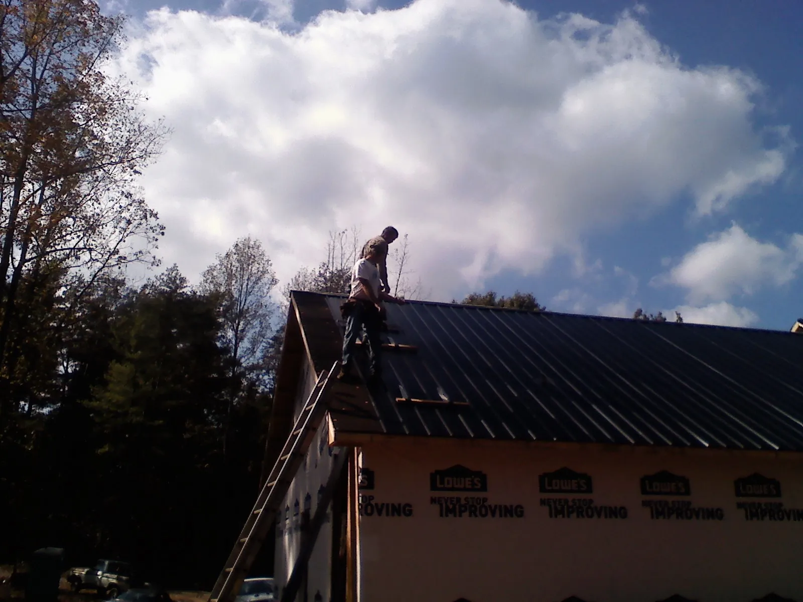 Roofer fastening dark metal panels high against a cloudy sky, from a Roof Inspection job in Gwynedd