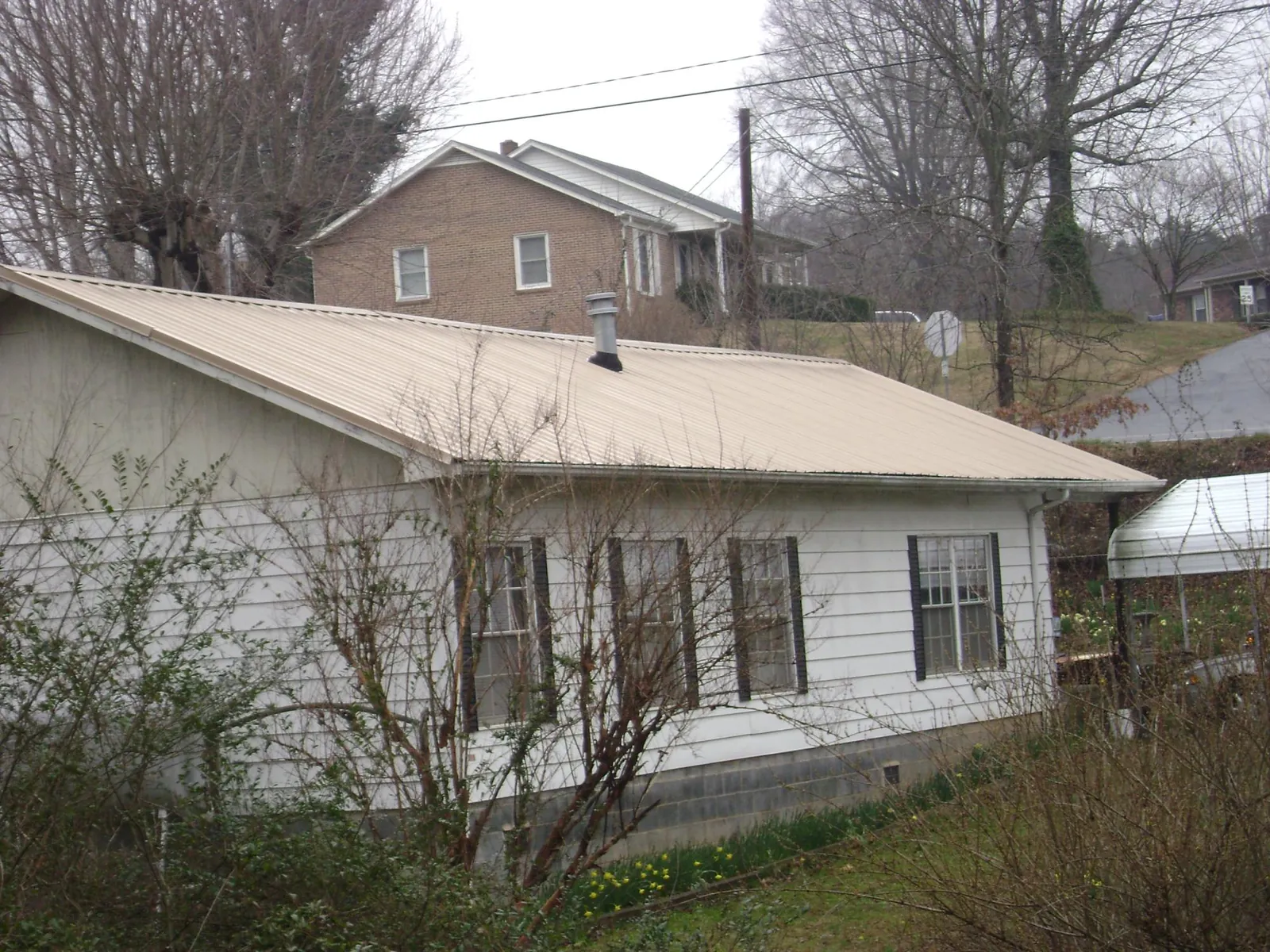 Tan metal roof on a white sided house set into a hillside — Commercial Roofing by Roofing Brothers in Gwynedd