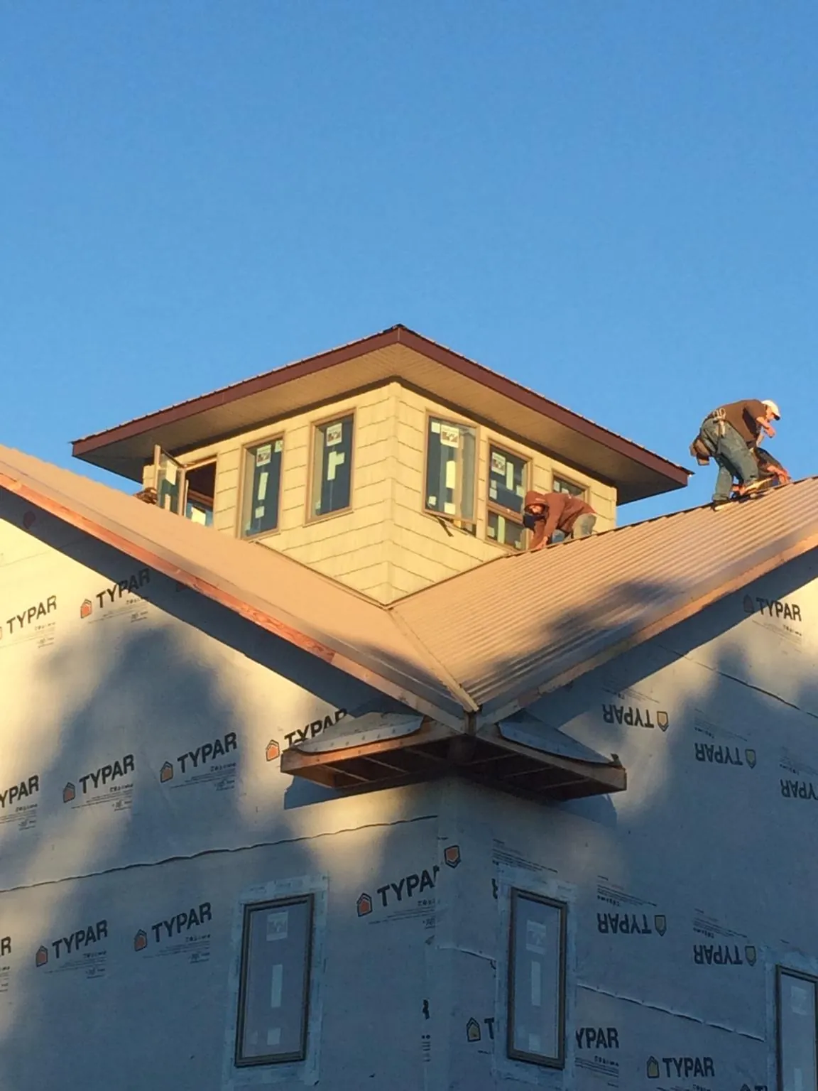 Roofers working around a rooftop cupola on a new metal roof at sunset — Roof Waterproofing in Gwynedd by Roofing Brothers